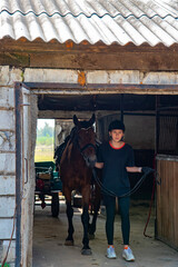 A teenage girl leads a horse out of the stable.
