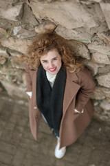 Portrait of a beautiful young woman near a stone wall. He looks up into the camera with a smile. Outside. View from above