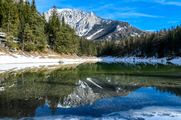 Fototapeta na wymiar Winter landscape of Austrian Alps with Green Lake in the middle. Powder snow covering the mountains and ground. Soft reflections of Alps in calm lake's water. Winter wonderland. Serenity and calmness