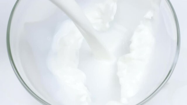 Close-up delicious natural milk is poured into glass bowl in slow motion, organic food and fresh drink concept, white background. White liquid, healthy eating, soya rice coconut skim milk, nutrition