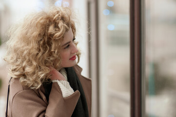 Fototapeta premium Young beautiful woman looks into a glass showcase. Blue bokeh. Outside