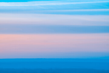 Varicolored striped surreal sky with shades of blue, cyan, pink colors with land. Horizontal lines of smooth clouds. Atmospheric background image of tender sky.