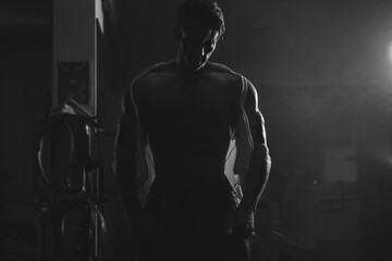 Fototapeta na wymiar silhouette of muscular man. Silhoutte of muscular man showing his body in ripped white shirt in gym. Monochrome. Cinematic style portrait.