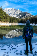 Fototapeta na wymiar A man walking around the shore of Green Lake, Austria. Powder snow covering the mountains and ground. Soft reflections of Alps in calm lake's water. Winter landscape of Austrian Alps. Calmness