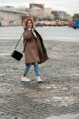 Beautiful brunette young woman in a red hat, jeans, and a coat happily walks along the street