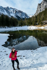 A woman walking around the shore of Green Lake, Austria. Powder snow covering the mountains and ground. Soft reflections of Alps in calm lake's water. Winter landscape of Austrian Alps. Calmness