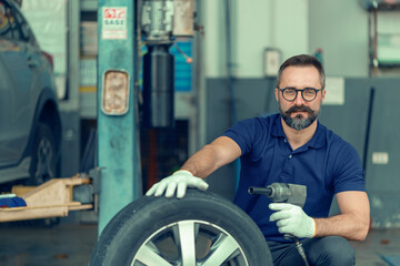 Obraz na płótnie Canvas Portrait of a man in professional look sitting and holding a tool/tires in the background of a car service centre concept