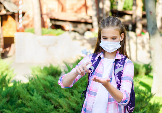 Cute little girl child with face mask and sanitizer in the park. Preteen student disinfecting hands after school outdoors. Education concept.