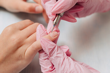 Manicure process. A master in pink rubber gloves polishes nails with an electric nail file. Female hands close up.