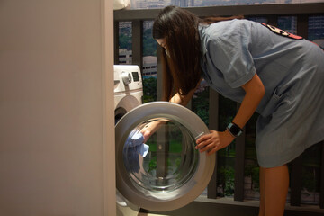 Young asian pregnant woman loading cloth into washing machine.