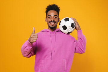 Happy african american guy showing thumb up while posing with football