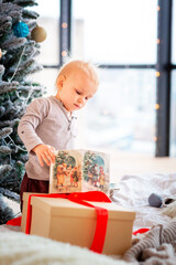 Fototapeta na wymiar Happy little baby boy opening present boxes near Christmas tree