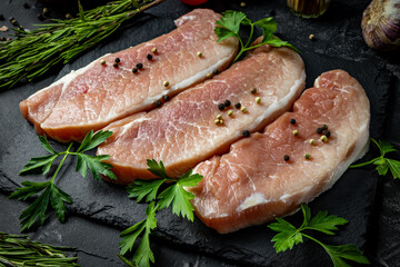  Pieces of raw pork meat with seasonings for its preparation on a black background, top view, close up