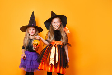 Portrait of two funny little girls dressed up as halloween witch on orange background