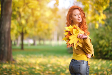 Cute redhaired woman holding autumn leafs in the natur