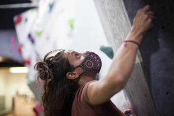 young fit woman climber wearing mask climbing on artificial wall indoors.