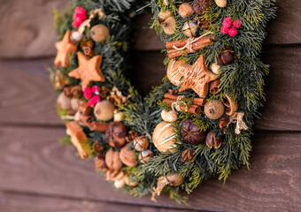 Traditional Christmas wreath made of fir branches, decorated with ginger cookies, cinnamon, nuts, berries, bells and a beautiful bow