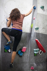 Obraz na płótnie Canvas young fit woman climber moving up on rock wall, climbing on artificial wall indoors.