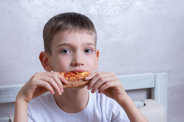 Cute boy eating a slice of pepperoni and cheese pizza, close-up, copy space. Unhealthy food concept