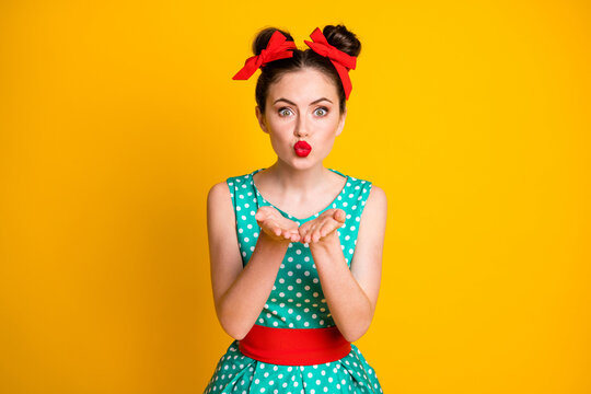 Portrait of glamorous lovable girl wearing dotted dress sending air kiss isolated over vibrant yellow color background