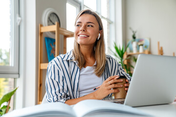 Young woman in earphones studying with laptop and book at classroom