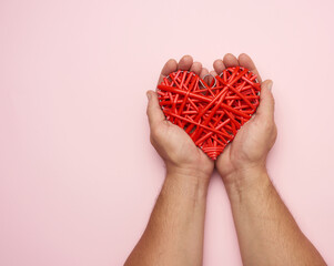 two male hands holding a red wicker heart on a pink background,