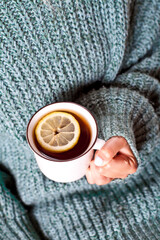 Female hands holding mug of hot tea with lemon in morning.