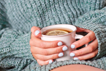 Female hands holding mug of hot tea with lemon in morning.