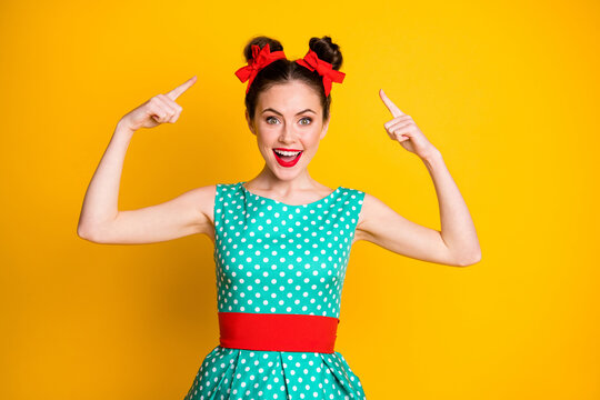 Portrait of nice amazed cheery girl wearing teal dotted dress showing new hairdo isolated over vibrant yellow color background