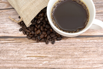 Top view of coffee beans and white cup of black coffee on wooden background