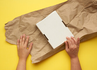 rectangular white cardboard box and two female hands are wrapped with brown paper