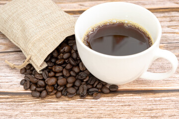 close up coffee beans and white cup of black coffee on wooden background