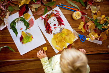 Toddler blond child, creating woman portrait of leaves in living room, applying leaves using glue