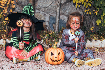 Two girls dressed as witch and zombie eating candy celebrating Halloween in the garden next to Jack...