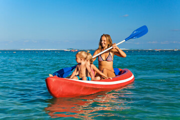 Happy family - young mother, children have fun on boat walk. Woman and child paddling on kayak. Travel lifestyle, parents with kids recreational activity, watersports on summer sea beach vacation.