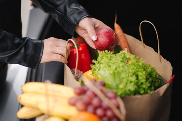 Close-up of groceries in eco package in car trunk. Hands of female packing vegetables and fruits after shipping in supermarket