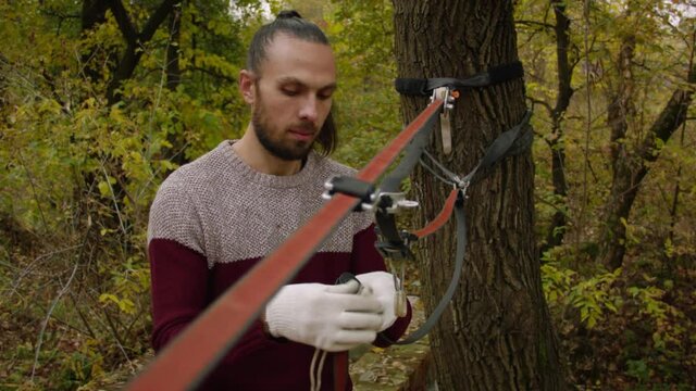 Caucasian man sets slackline between trees in the autumn forest. A man practices highlining in the autumn. 