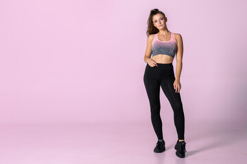 Fototapeta na wymiar Young athletic woman standing in fitness outfit with ponytail in front of a pink background