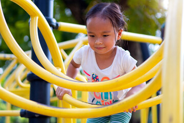 Asian girl is climbing on a playground equipment in a school.