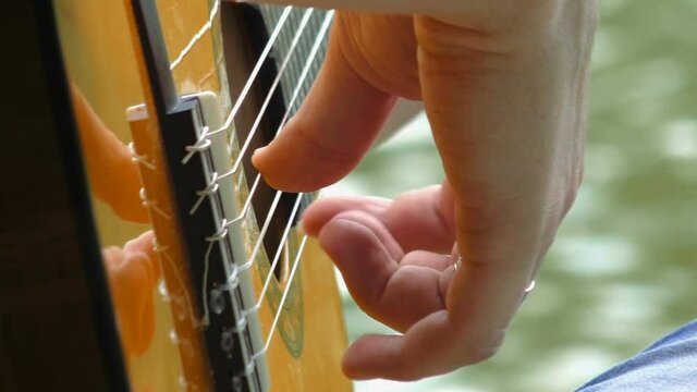 Close up fingers of the right male hand playing acoustic guitar outdoors