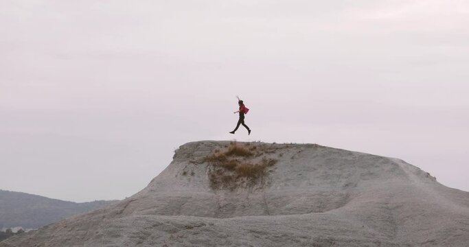 Happy Man wearing skull cap and red shirt running to the top of a grey rocky mountain and jumping victorious. Feeling successful and happy. Personal achievement goal succeed concept.