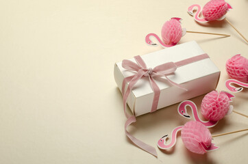 Decorative flamingos and white gift box with pink bow on the beige surface.Empty space