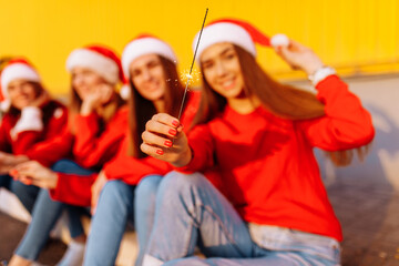 Obraz premium Company of cheerful young women celebrating the New Year in Santa Claus hats, with sparklers