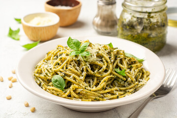 Spaghetti pasta with pesto sauce, parmesan cheese and basil leaves in plate on concrete background