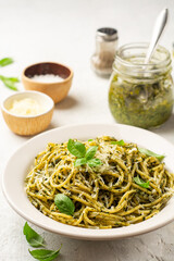 Spaghetti pasta with pesto sauce, parmesan cheese and basil leaves in plate on concrete background