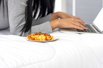 Pizza with a long haired woman lying on her laptop, searching for information, working or playing games on the Internet. (Work from home concept)