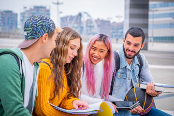 Multiethnic students joking and talking sitting on the bench together outdoors in a university - Group of happy young teenagers studying with books and tablets