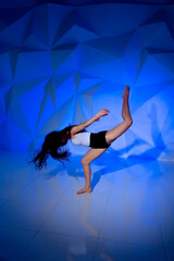 Woman dancing on the background of a beautiful multicolored wall. Sexy slim lonely girl with long black hair. female holds her head. bright colorful geometry background.