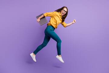 Fototapeta na wymiar Full length profile photo of lady jump run hold netbook wear yellow shirt blue pants sneakers isolated purple color background