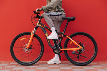 Close photo of woman's legs and bicycle on red background. Cropped photo of woman standing on bicycle on red wall background.
